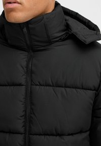 Black puffer jacket with a high collar and zip closure. Features quilted padding, smooth texture, and a detachable hood.