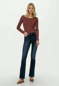 Top de manga larga color burdeos combinado con jeans de campana azul oscuro, con una cintura alta y una silueta ajustada. La modelo lleva tacones marrones.