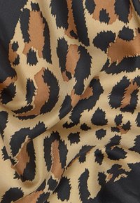 Tissu à motif léopard avec des taches irrégulières noires, brunes et beiges sur une surface lisse et légèrement froissée.