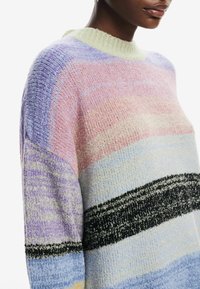 Pull léger en maille texturée avec des couleurs pastel : rose, lavande, bleu, et une rayure horizontale noire. Encolure ronde, coupe ample.
