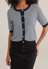 Marinblå och vit randig kortärmad cardigan med rund halsringning och knappstängning, tillsammans med en svart denimkjol.