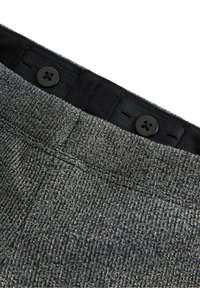 Grå tekstureret stoftalje med sort elastik, prydet med to sorte knapper og synlige sømdetaljer, designet til skræddersyede bukser.