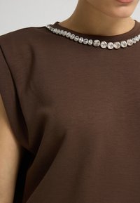 Hnědý krátký rukáv top vyrobený z hladké tkaniny, s límcem zdobeným jasnými rhinestony v symetrickém vzoru.