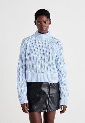 Pull en tricot bleu clair avec un col haut, ourlet côtelé et motif texturé, associé à une mini jupe en cuir noir avec une fermeture éclair à l'avant.