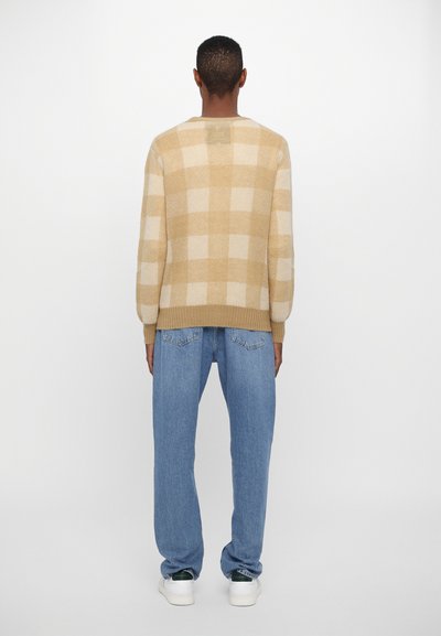 Beige och gräddfärgad rutmönstrad tröja i stickad tyg, med ribbade muddar och nederkant, i kombination med ljusblå avspända jeans.