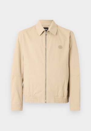 Beżowa kurtka zapinana na zamek z kołnierzem, długimi rękawami, elastycznym dołem, bocznymi kieszeniami i małym okrągłym logo na lewej piersi.