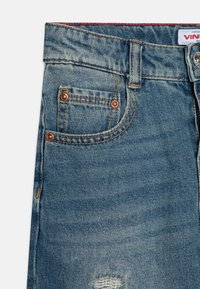 Denimbukser med lys vask, med kobberfargede metallknapper, en liten frontlomme og slitt detaljer på stoffet.