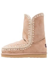 Beige semsket støvel med hvit flette-søm, rund tå og lav profil. Myk tekstur med flat gummisåle. Ingen synlige logoer.