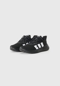 Baskets de sport noires avec une tige en mesh, motif à trois bandes blanches sur le côté, et semelle en caoutchouc texturé noire. Lacets lumineux avec un motif.