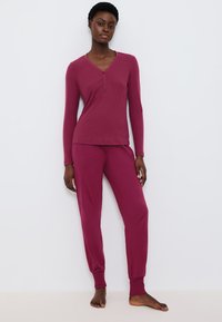 Paarse langemouw henley-top met knopen, gecombineerd met bijpassende jogger pants. Soepele stof; strakke pasvorm; geribbelde textuur op de top.