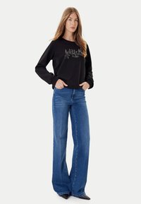 Felpa nera con testo ricamato e design floreale, abbinata a jeans denim a gamba larga azzurri e scarpe nere con punta appuntita.