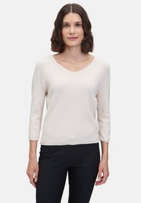 Hellbeige geripptes Blusenshirt mit V-Ausschnitt und Dreiviertelärmeln, aus weichem Stoff gefertigt, kombiniert mit schwarzen, figurbetonten Hosen.