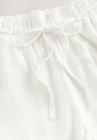 Biele ľanové nohavice s elastickým pásom a zozelenou šnúrkou na prednej strane, zobrazené zblízka.