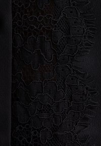 Tessuto nero con un intricato design floreale in pizzo con dettagli testurizzati, che passa da una superficie liscia a un motivo a rete.