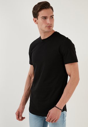 T-shirt nera a girocollo, maniche corte, design aderente, realizzata in tessuto di cotone liscio, abbinata a jeans blu chiaro.