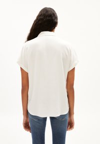Witte blouse met korte mouwen, een kraaghalslijn, een gladde textuur en een ronde zoom, gedragen met blauwe jeans.