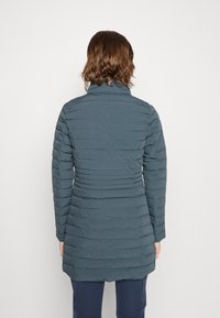 Polstret teal-frakke med høj krave og struktureret bølgemønster. Lange ærmer strækker sig til en lige skæring, der når til midt på låret.