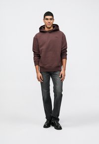 Καφέ φούτερ με κουκούλα και μπροστινή τσέπη, συνδυασμένο με σκούρο γκρι τζιν παντελόνι και μαύρα παπούτσια. Απλός σχεδιασμός, μεσαία υφή και άνετη, καθημερινή εφαρμογή.