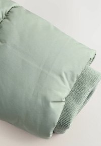 Jasnozielona kurtka puchowa z gładkim wykończeniem materiału i prążkowanymi mankietami. Starannie złożona, ukazująca swoją miękką teksturę i design.