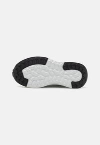 Potplat cipela ima crne gumene rebraste trake, teksturirani bijeli međupotplat i geometrijske uzorke za bolje prianjanje. Izdržljiva konstrukcija dizajnirana za visoke performanse.