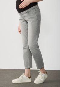 Jeans de maternidad grises con corte ajustado y cinturilla elástica, acompañados de zapatillas blancas. El denim tiene una textura suave y un acabado de lavado claro.