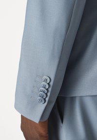Lichtblauwe colbertmouw met gladde stof, vijf ronde knopen en contrasterende stiksels. Schoon en nauwkeurig ontwerp.
