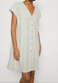 Ljusgrön linnetekstilklänning med V-ringning, korta ärmar och knapprad fram. Har en avslappnad passform och ett strukturerat tyg för god andningsförmåga.