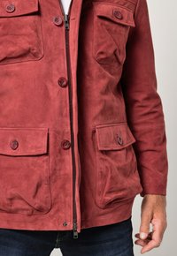 Rød ruskindsjakke med lynlås foran, knaplommer og tekstur. Indeholder tre lommer foran og lange ærmer.