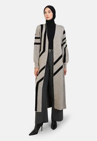 Long gray cardigan with black geometric stripes, knitted texture, open front, and balloon sleeves, paired with black top and wide trousers.