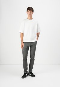 Weißes Kurzarm-T-Shirt, graue Slim-Fit-Hosen und schwarze Sneaker mit weißen Streifen. Glattes Material, klare Linien und minimalistisches Design.