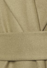 Beige wikkel van gestructureerde stof, met diagonale weefpatronen en een bijpassende riem, met een gevouwen ontwerp met gelaagde elementen.