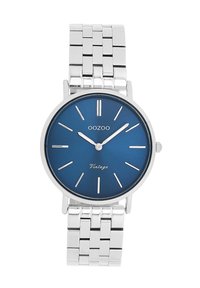 Montre ronde en argent avec un cadran bleu, des index horaires en argent et une inscription vintage. Dotée d'un bracelet en maillons métalliques.