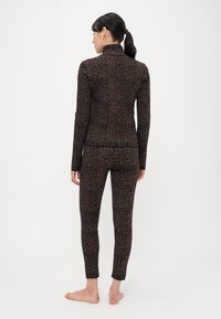 Top s leopardím vzorom s dlhým rukávom a priliehavé legíny v čiernej a hnedej farbe, s vysokým golierom a detailom s logom na páse.