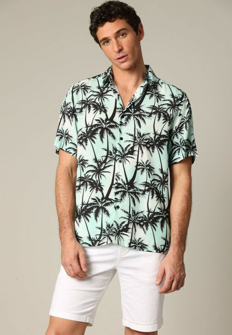 Korte mouwen button-up shirt in licht muntgroen met een zwart palmbomenpatroon. Gecombineerd met witte shorts, die een relaxte pasvorm en zachte textuur hebben.