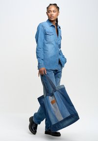 Helles blaues Jeanshemd mit zwei Brusttaschen, kombiniert mit passenden hellblauen Jeanshosen. Trägt eine große, mehrfarbige Jeans-Totebag.