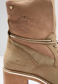 Bottine en cuir fauve avec détails cousus, logos Tom Tailor embossés et talon épais en bois.