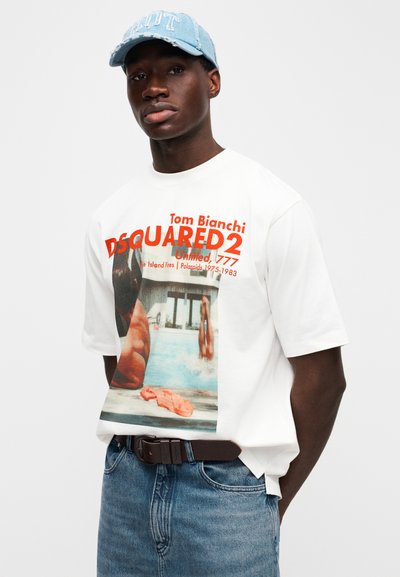 Λευκό κοντομάνικο μπλουζάκι με φωτογραφική εκτύπωση κολυμβητή, με κόκκινο κείμενο «DSQUARED2» και καφέ ζώνη πάνω από μπλε τζιν. Ανοιχτό μπλε καπέλο.