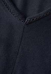 Tmavě námořnická látka s výstřihem do V, která má texturovaný šev podél výstřihu a hladký, rovnoměrný povrch.