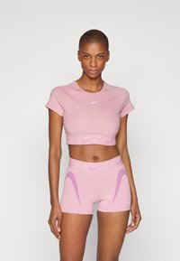 Lys rosa atletisk crop topp og shorts med en teksturert midje. Har Nike-logo og skrå lilla detaljer på shortsene.