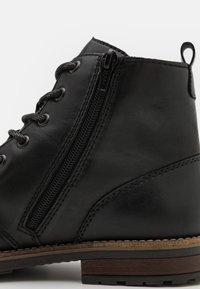 Botas de cuero negras a media caña con cremallera lateral, puntera redondeada y suela de madera contrastante con detalles de costura texturizada.