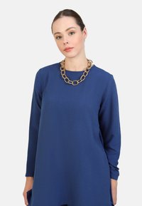 Blue long-sleeve dress made of textured fabric, featuring a round neckline. Accented with a chunky gold chain necklace. Simple design.