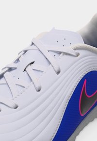 Približna snimka vezica bijele tenisice vezanih na plavom bočnom panelu s crnim Swoosh logotipom obrubljenim ružičastom bojom, prikazujući teksturiranu površinu cipele i perforacije.