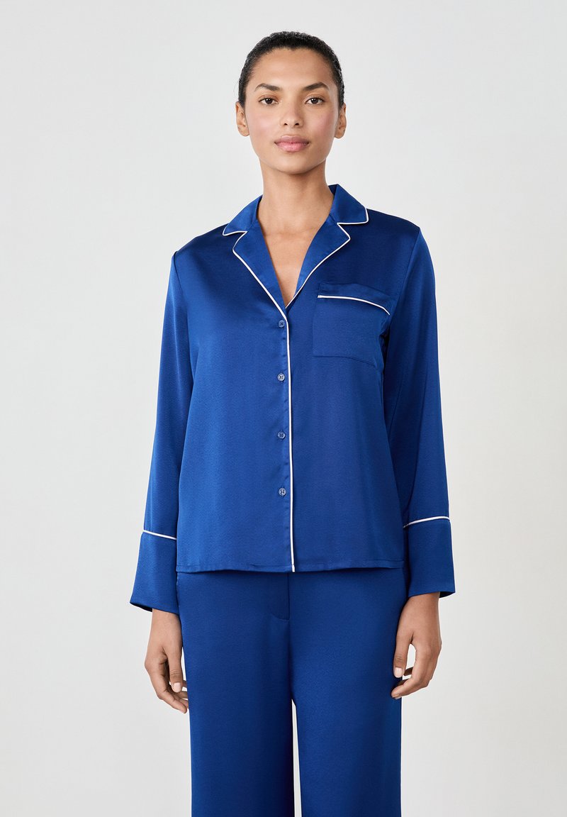 Ensemble de pyjama en satin bleu avec une chemise à boutons, des passepoils blancs et des manches longues. Présente une poche poitrine et un pantalon assorti. Textile lisse.