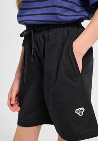 Svarta bomullsshorts med elastisk midja och dragsko, sidofickor och en beige broderad logotypdetalj på nedre benet.