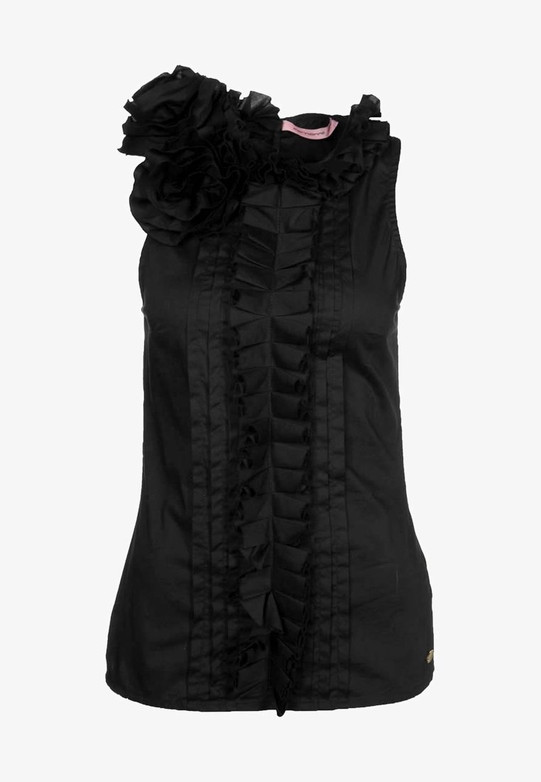 Blouse noire sans manches avec des volants verticaux sur le devant et une grande fleur en tissu sur l’épaule gauche.