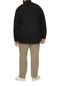 Schwarzer Strickpullover mit hochgeschlossenem Kragen, Raglanärmeln und geradem Schnitt, kombiniert mit beigen Hosen und weißen Sneakern.