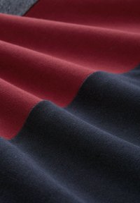 Textielstof in diep rood en donkerblauw, met een zachte, gestructureerde oppervlakte met gladde, golvende plooien die visuele diepte creëren.