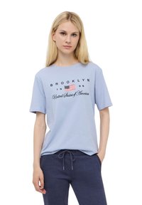 T-shirt di cotone blu chiaro con grafica nera "BROOKLYN 1996" e una piccola bandiera americana. Maniche corte e vestibilità rilassata. Abbinato a pantaloni jogger grigi scuri.