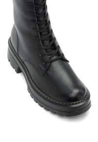 Bottines de combat en cuir noir à lacets, avec une épaisse semelle en caoutchouc et une finition texturée, présentées sous un angle supérieur avant.