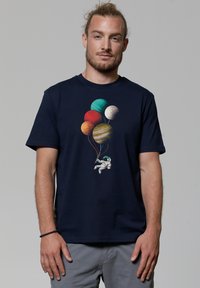 T-shirt en coton bleu marine avec un graphisme d'astronaute tenant des ballons de planète colorés dans différentes nuances. Manches courtes, coupe décontractée.